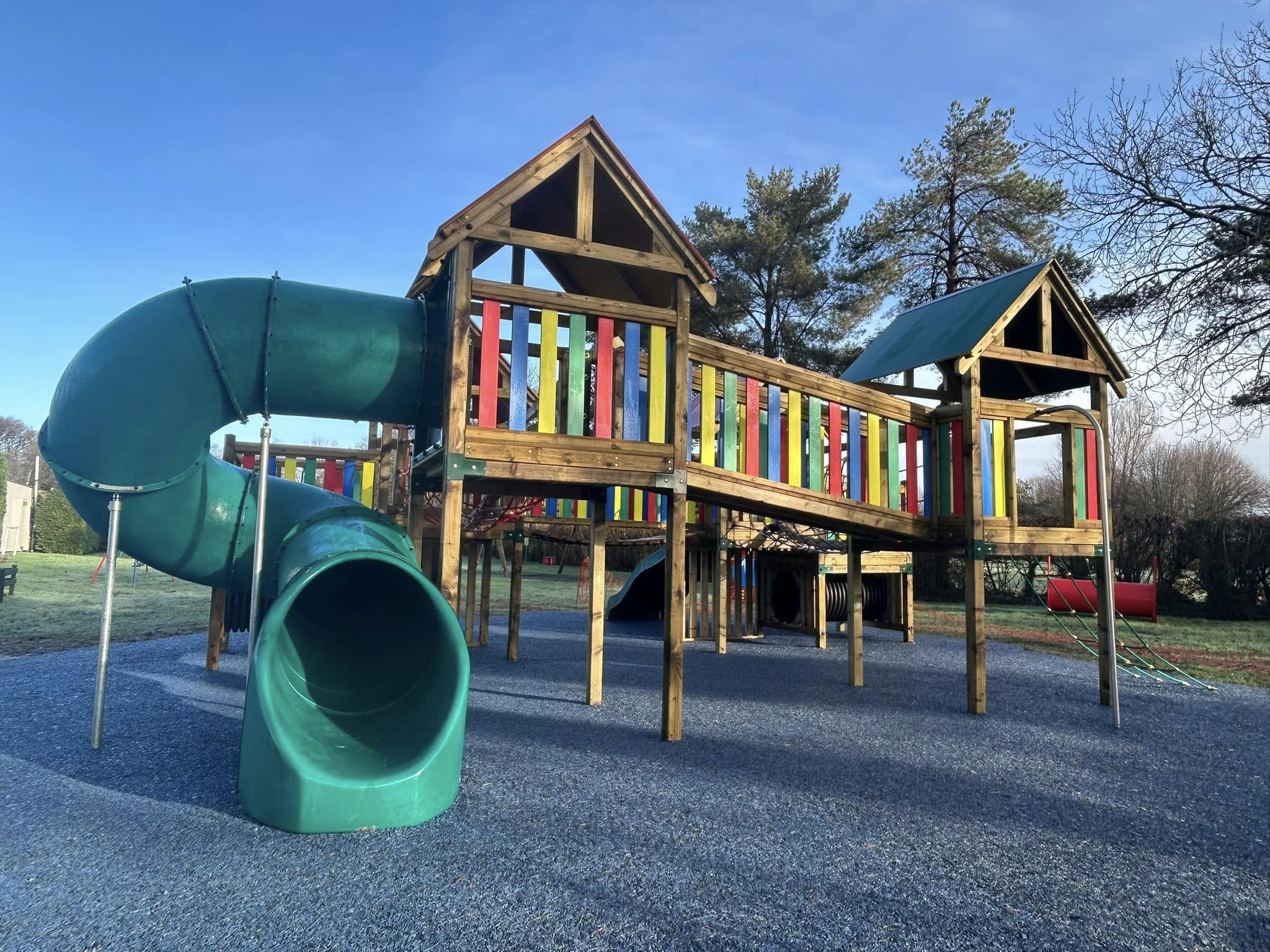 A green tube slide curving down from a wooden climbing frame at the play park