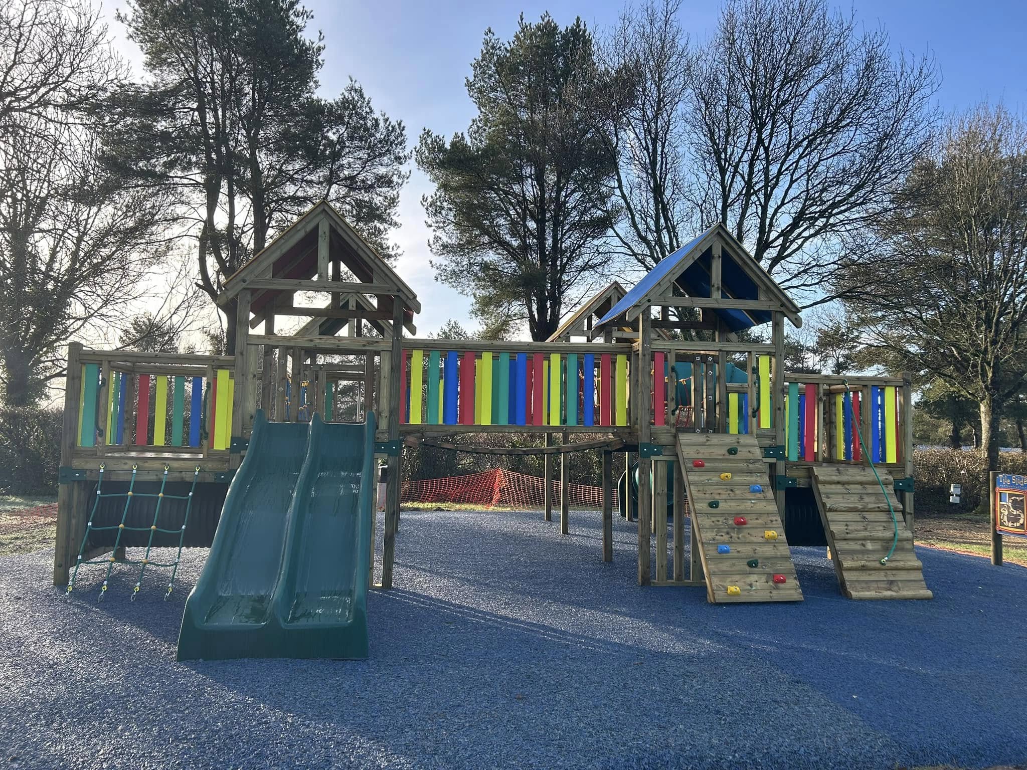 Wooden climbing frames with slides and coloured panels on a safety surface at the play park